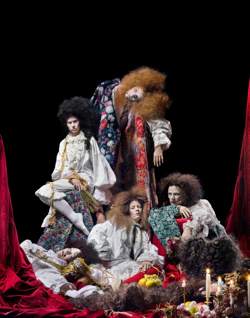 Fyra personer poserar i barockklädsel och stora peruker